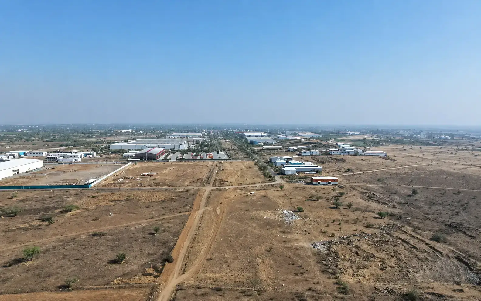 Aerial drone view of wide access roads, large industrial manufacturing plants, and warehouses in the Ranjangaon MIDC industrial area.